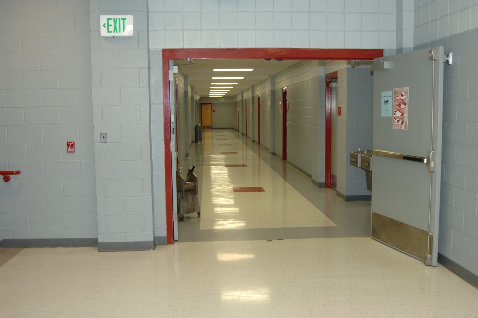 School hallway with white walls, red trim, and exit sign